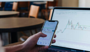 Person vor Laptop mit Investmentcharts – analysiert aktuelle Markttrends am Smartphone.