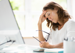 Dienstunfähigkeitsversicherung für Beamte - Beamtin sitzt am Schreibtisch, stützt den Kopf in den Arm und zeigt erschöpften Gesichtsausdruck.
