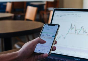 Person vor Laptop mit Investmentcharts – analysiert aktuelle Markttrends am Smartphone.