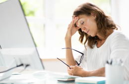 Beamtin sitzt am Schreibtisch, stützt den Kopf in den Arm und zeigt erschöpften Gesichtsausdruck – Symbol für Dienstunfähigkeit